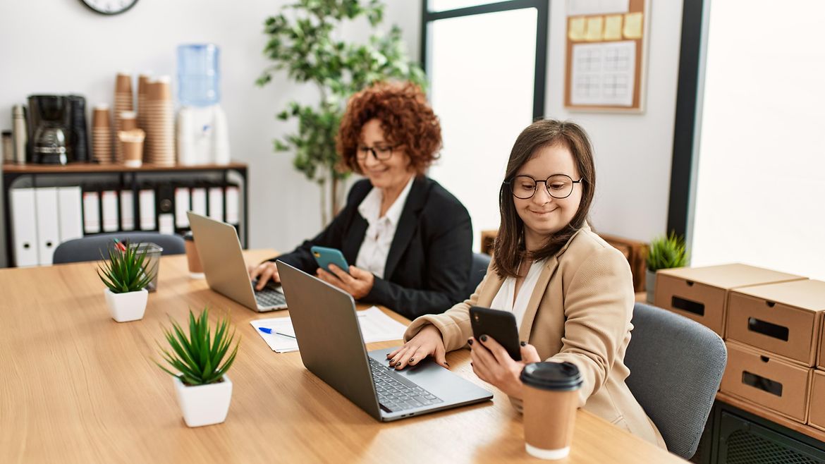 Inklusion am Büroarbeitsplatz Zwei Frauen arbeiten im Büro, eine mit Down-Syndrom.