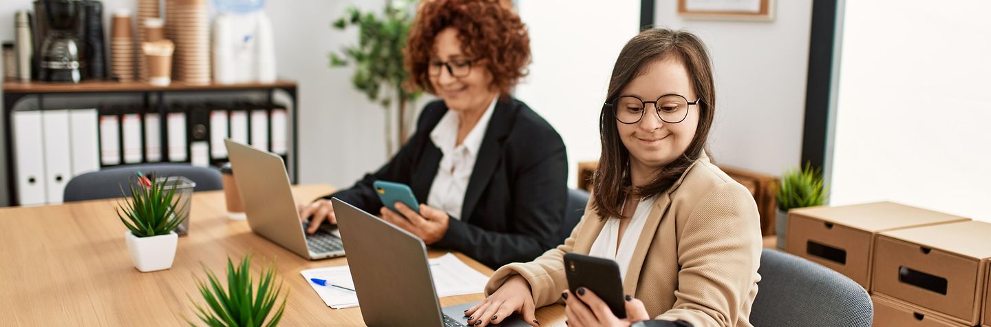 Inklusion am Büroarbeitsplatz Zwei Frauen arbeiten im Büro, eine mit Down-Syndrom.