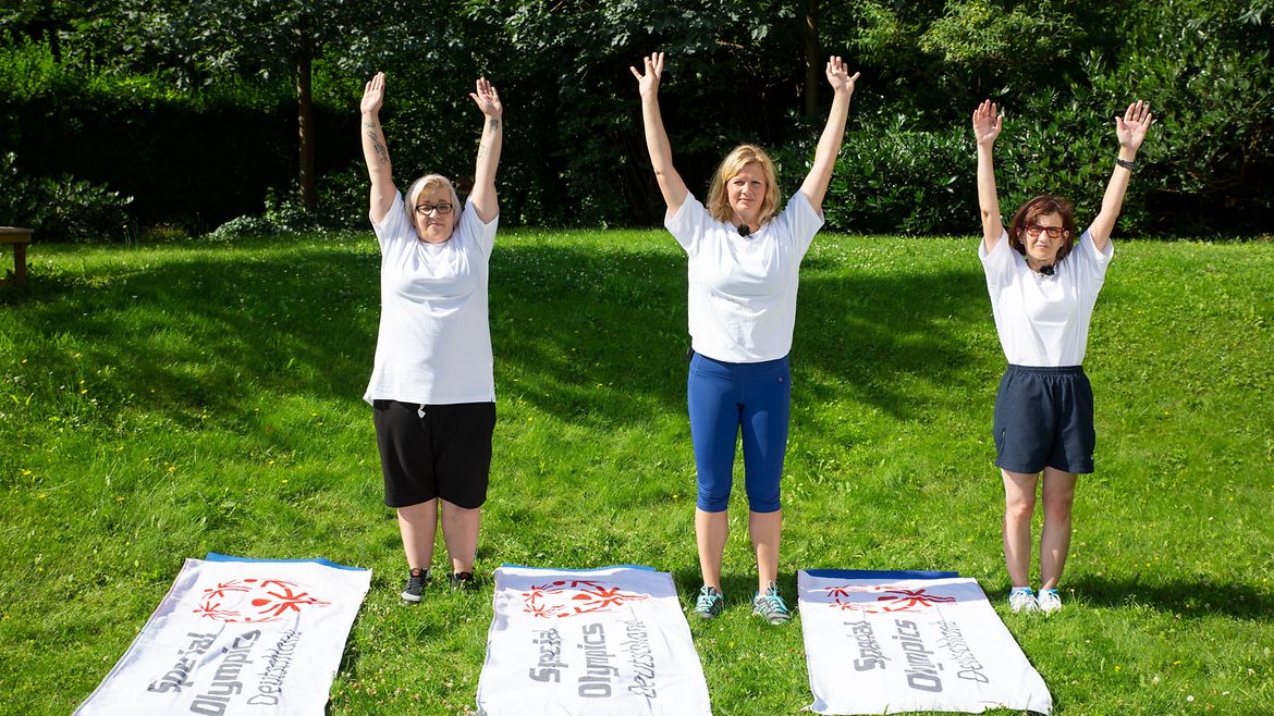 Drei Frauen machen auf einer Wiese gemeinsam Sportübungen.