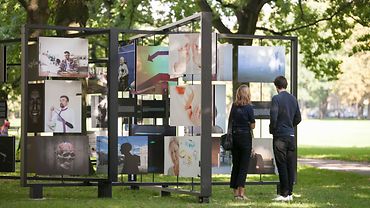 Zwei Personen auf einer Open-Air-Fotoausstellung, die auf großen drehbaren Tafeln präsentiert wird