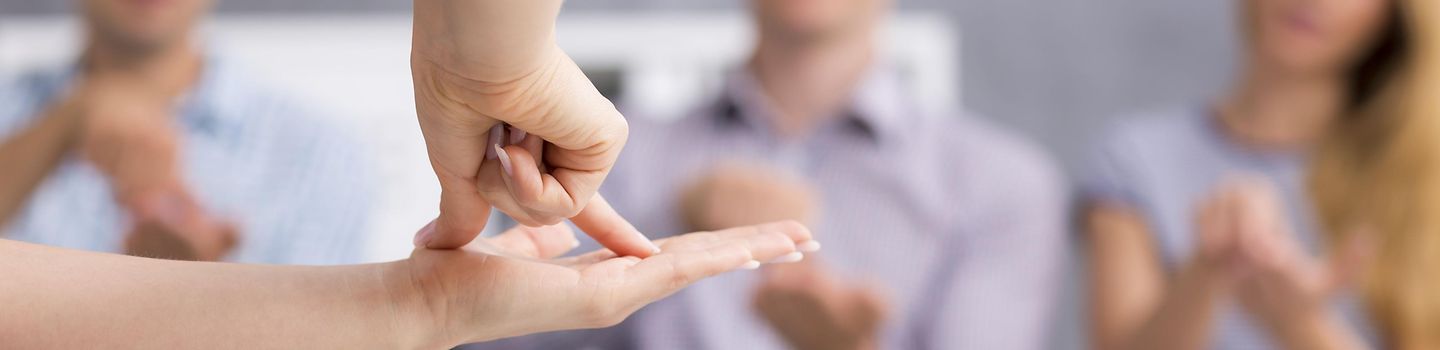 Gebärdensprache Im Vordergrund zeigt eine Hand einen Begriff in Gebärdensprache für drei andere Personen.