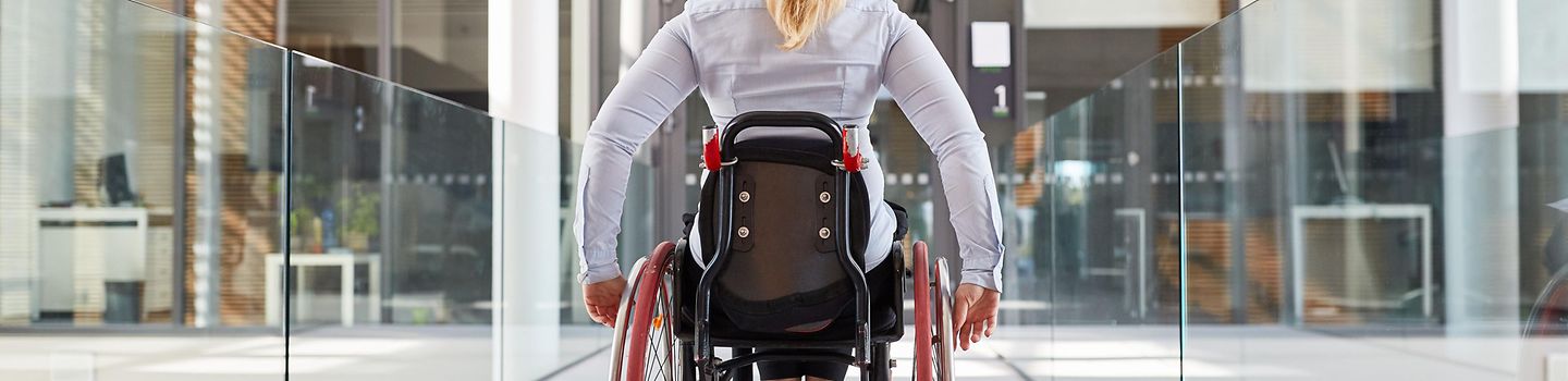 Frau im Rollstuhl ist unterwegs in einem barrierefreien Bürohaus.