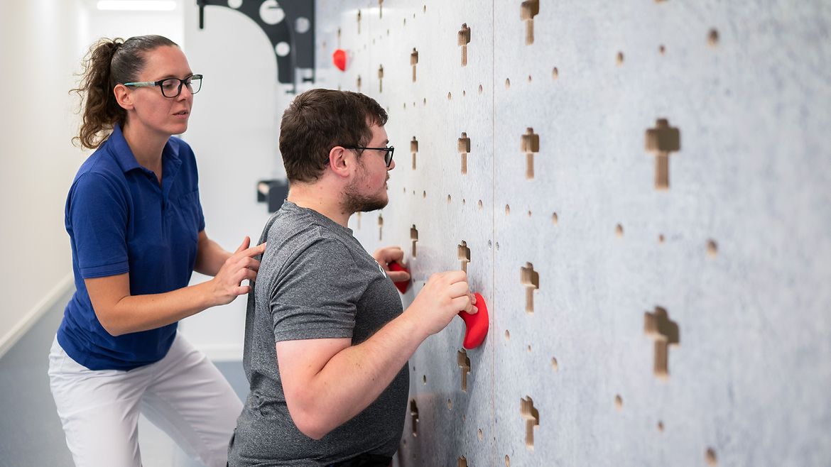 Eine Trainerin korrigiert die Körperhaltung eines jungen Mannes an der Kletterwand.