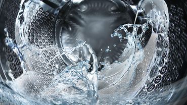 Reinigung Arbeitskleidung Blick in die laufende Trommel einer Waschmaschine mit Wasser.