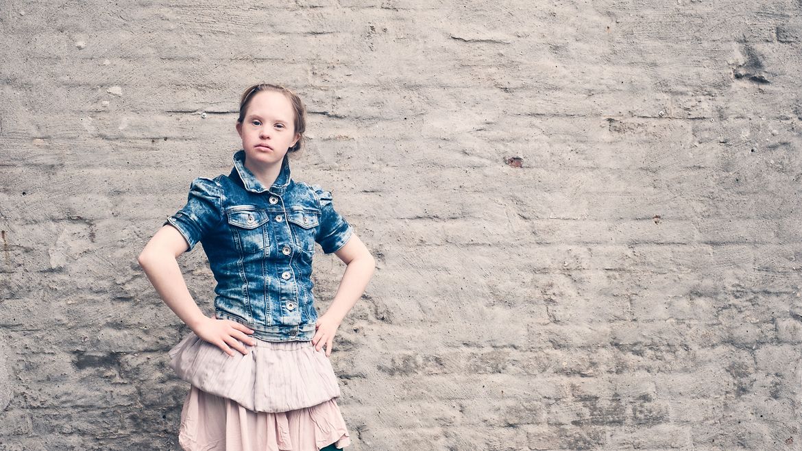 Ein junges Mädchen in Rock und Jeansjacke vor einer alten Hauswand.