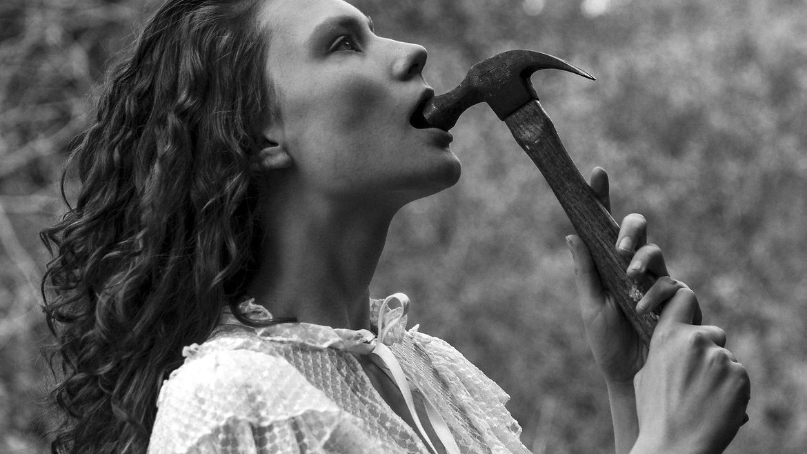 Eine Junge Frau steckt sich einen Zimmermannshammer in den Mund.