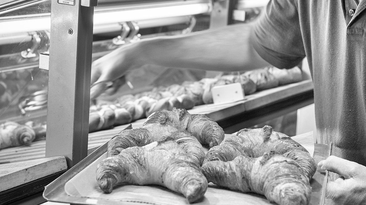 Ein junger Mann mit Mundschutz legt Croissants in einen Verkaufstresen.