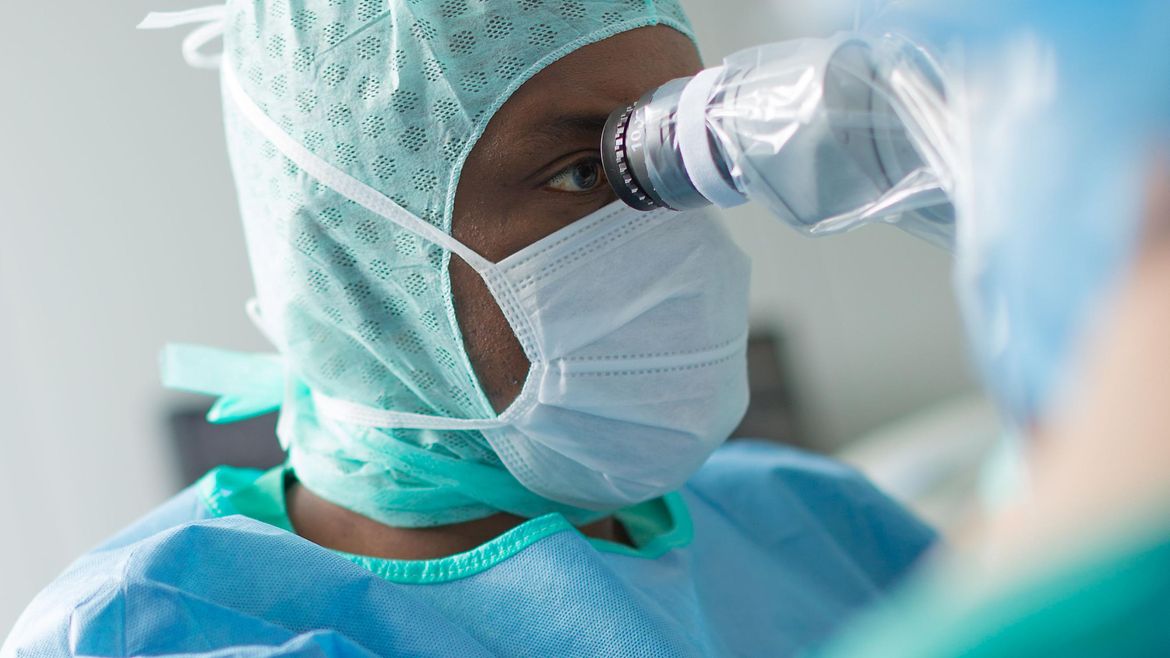 Ein Neurochirurg bei der Arbeit im OP - er schaut in ein Mikroskop.