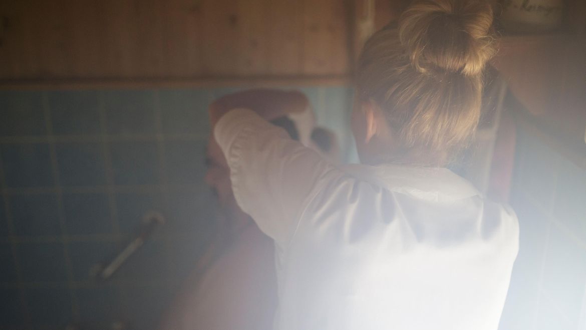 Eine Pflegerin wäscht einem Mann in einer Badewanne die Haare.