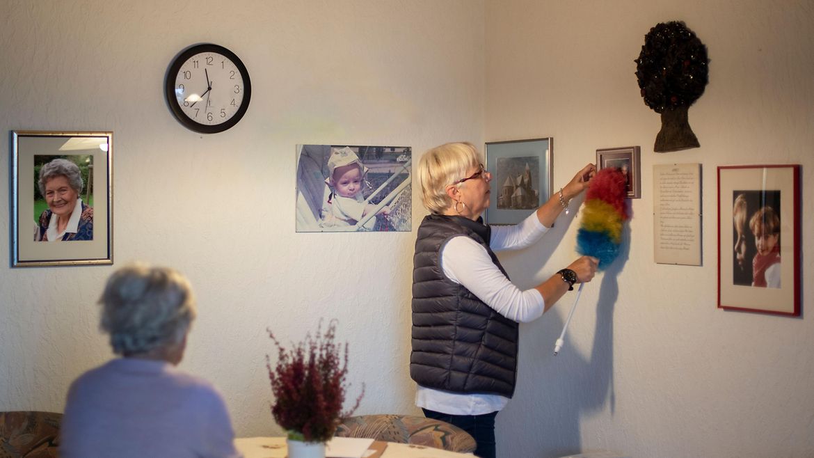 Eine ältere Frau entstaubt Bilderrahmen.