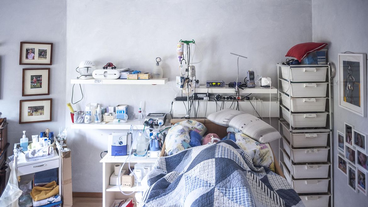 Ein älterer Mann liegt in einem Bett, umgeben von medizinischen Geräten.