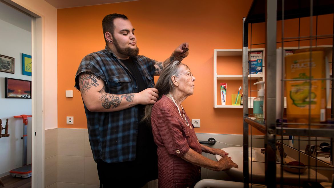 Ein Pfleger kämmt einer älteren Frau die Haare.