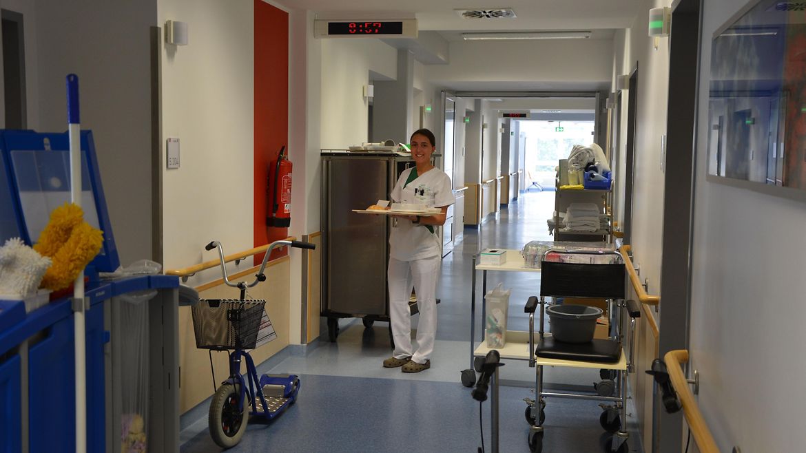 Eine Pflegerin steht mit einem Tablett in einem Krankenhausflur.