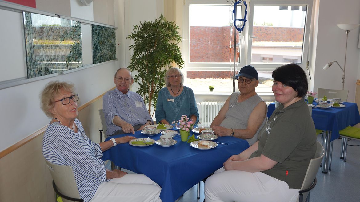 Fünf Personen sitzen um einen Tisch mit Kaffee und Kuchen.