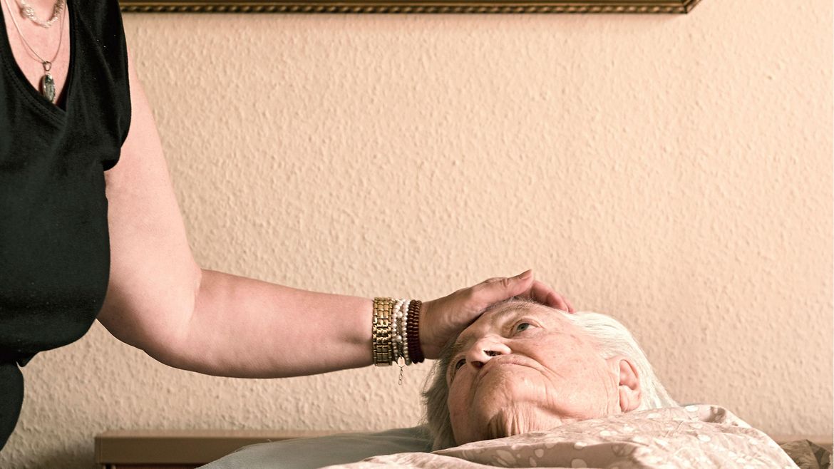 Eine Frau streichelt einer älteren Frau im Bett über den Kopf.