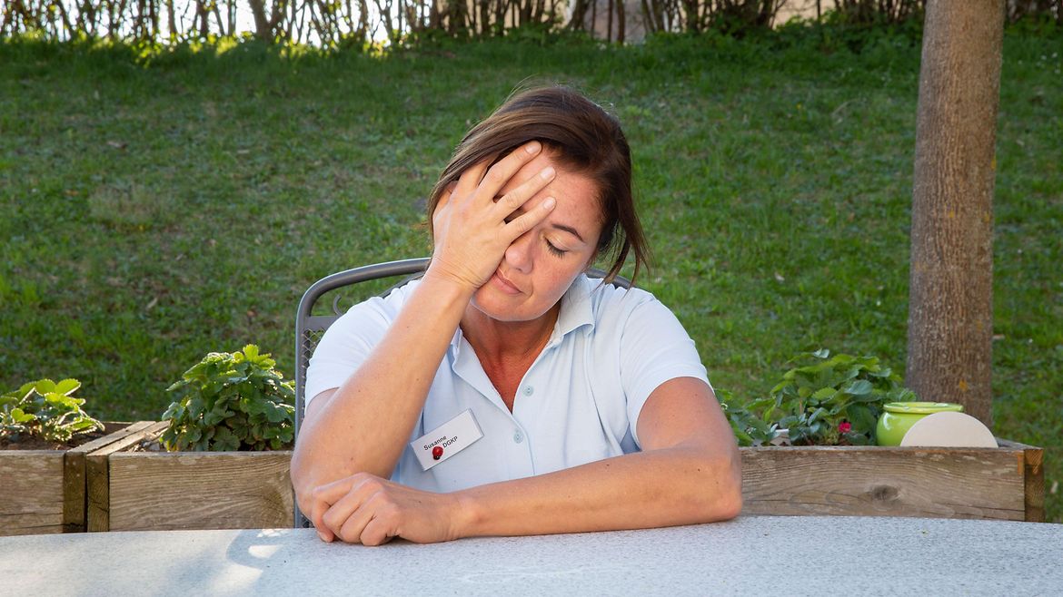 Eine Pflegerin sitzt erschöpft an einem Tisch in einem Garten.