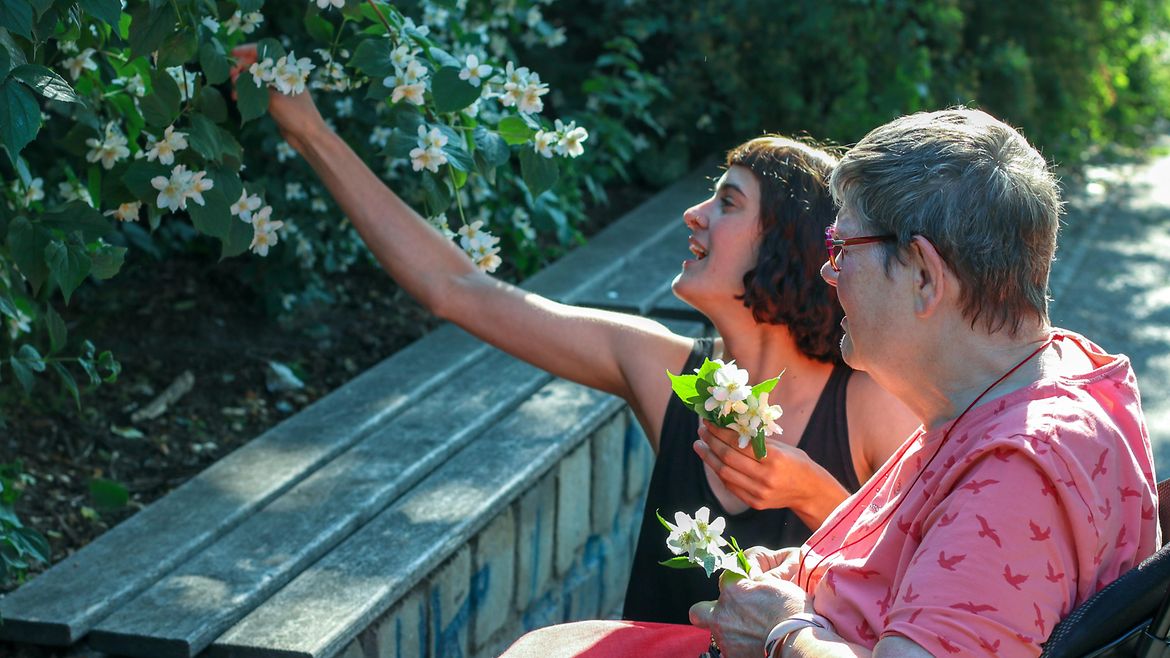 Eine junge Frau pflückt Blumen für eine ältere Frau im Rollstuhl.