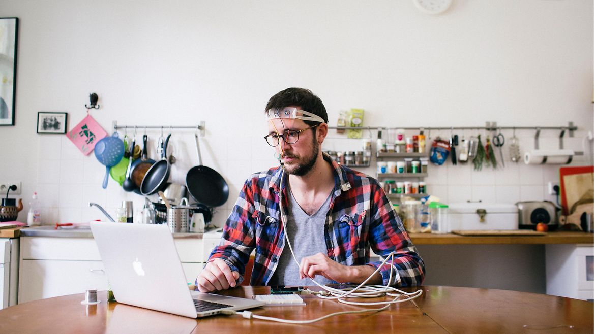 Ein Mann sitzt an einem Laptop und trägt ein Stirnband mit Elektroden am Kopf.