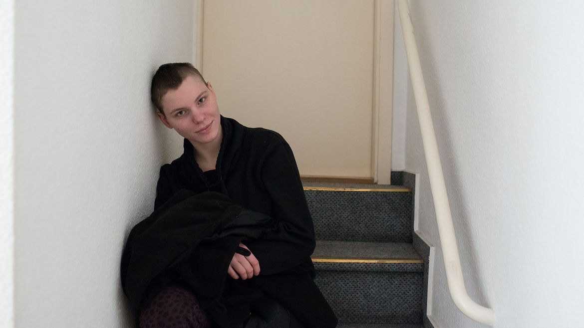 Eine junge Frau mit kurzem Haar sitzt lächelnd auf einer Treppe.