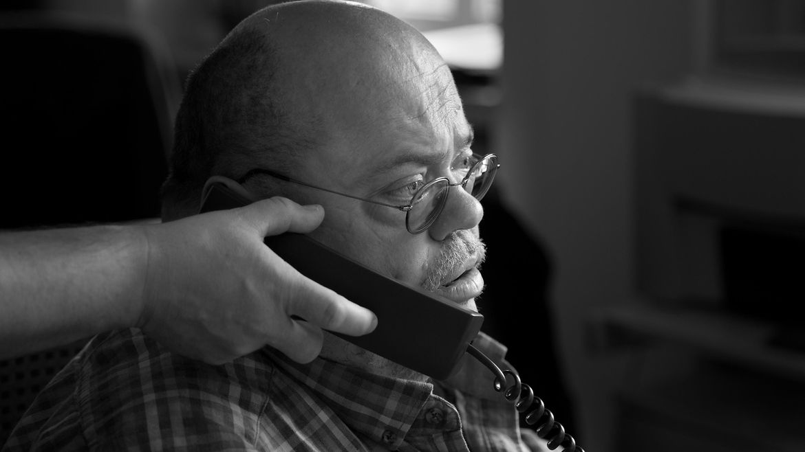 Eine Hand hält einem Mann einen Telefonhörer ans Ohr.