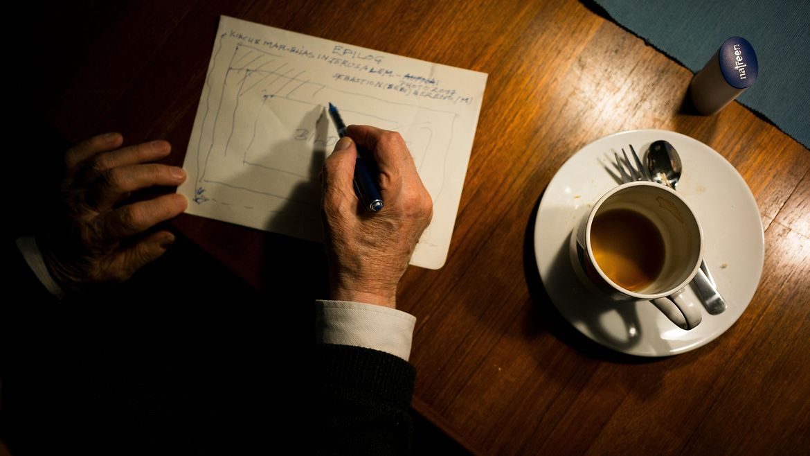 Hände auf einem Tisch zeichnen eine Skizze. Daneben steht benutztes Kaffeegeschirr.