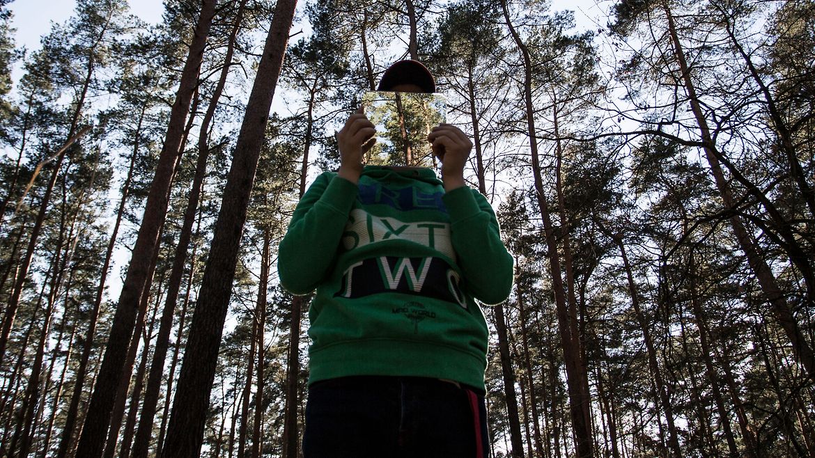 Ein Mann steht im Wald und hält ein Foto eines Waldes vor sein Gesicht.