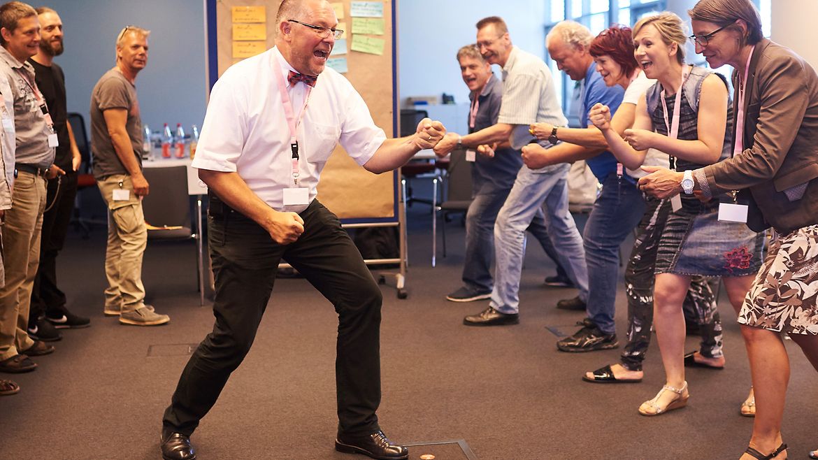 Workshop-Leiter steht vor einer Personen-Gruppe und macht eine Box-Bewegung - alle aus der Personengruppe machen die gleiche Bewegung. Alle rufen etwas.