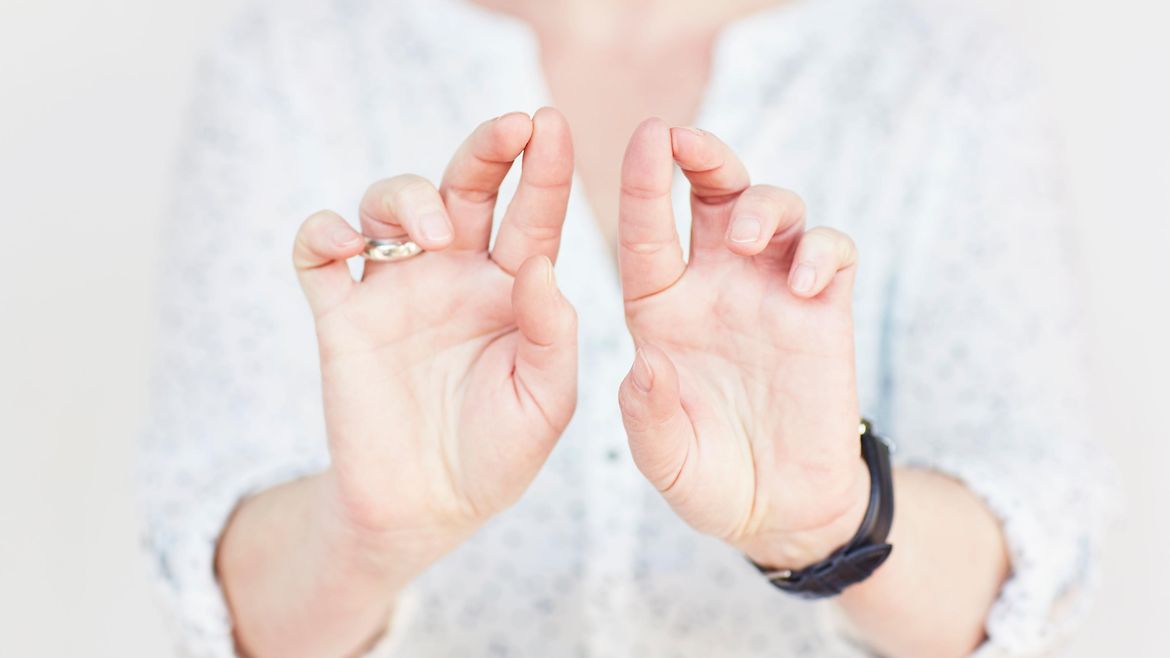 Die Hände einer Frau. Die Handinnenflächen sind der Kamera zugewandt, Zeige- und Mittelfinger jeder Hand sind nach oben gerichtet und berühren sich an den Spitzen.