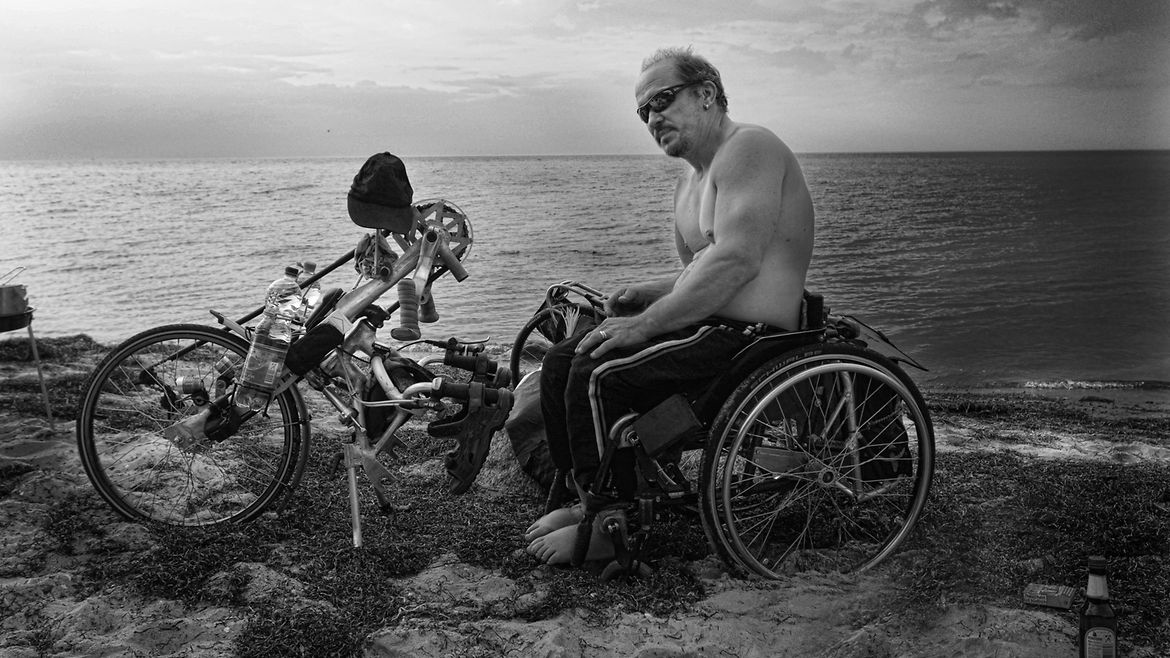 Ein Mann sitzt in einem Handybike am Meer.