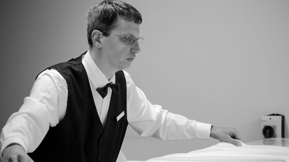 Ein schlanker Mann mit Brille legt ein weißes Tischtuch aus.