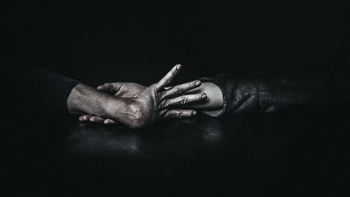 Zwei spastisch gelähmte Hände, die sich gegenseitig halten - vor schwarzem Hintergrund.