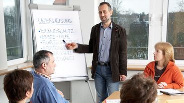 Schulung Schulung: ein Mann steht an einem Flipchart, mehrere Menschen hören ihm zu