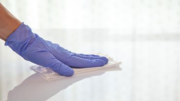 Hand mit blauem Handschuh wischt mit einem Tuch über eine glatte Fläche.