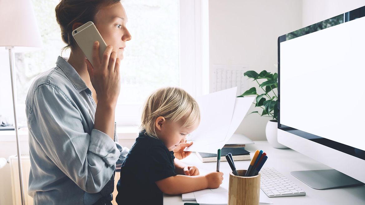 Frau mit Kind auf dem Schoß arbeitet zu Hause - sie telefoniert.