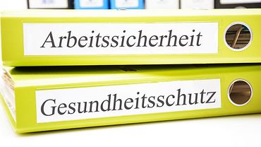 Zwei Aktenordner liegen aufeinander. Sie tragen die Aufschriften "Arbeitssicherheit" und "Gesundheitsschutz".