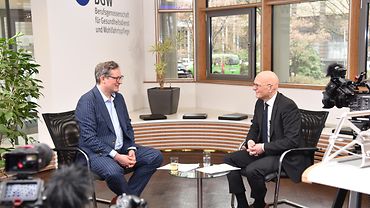  Dr. Eckart von Hirschhausen und BGW-Hauptgeschäftsführer Jörg Schudmann sitzen im Foyer der BGW-Hauptverwaltung und sprechen miteinander