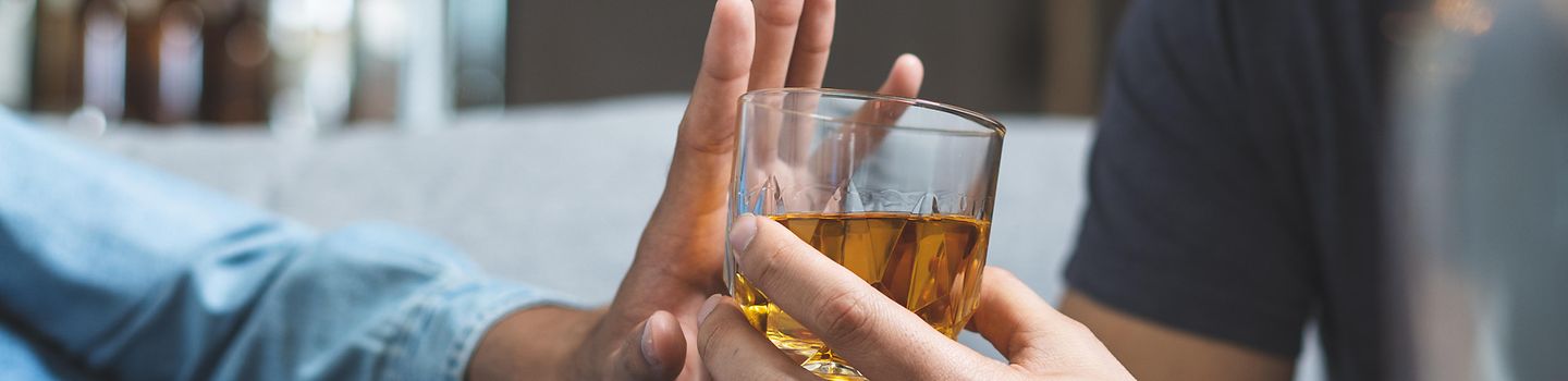 Eine Hand reicht einer Person ein volles Whiskyglas, sie wehrt mit der Hand ab.