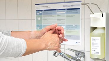 Händedesinfektion Hände bei der Desinfektion, im Hintergrund Händehygieneplan