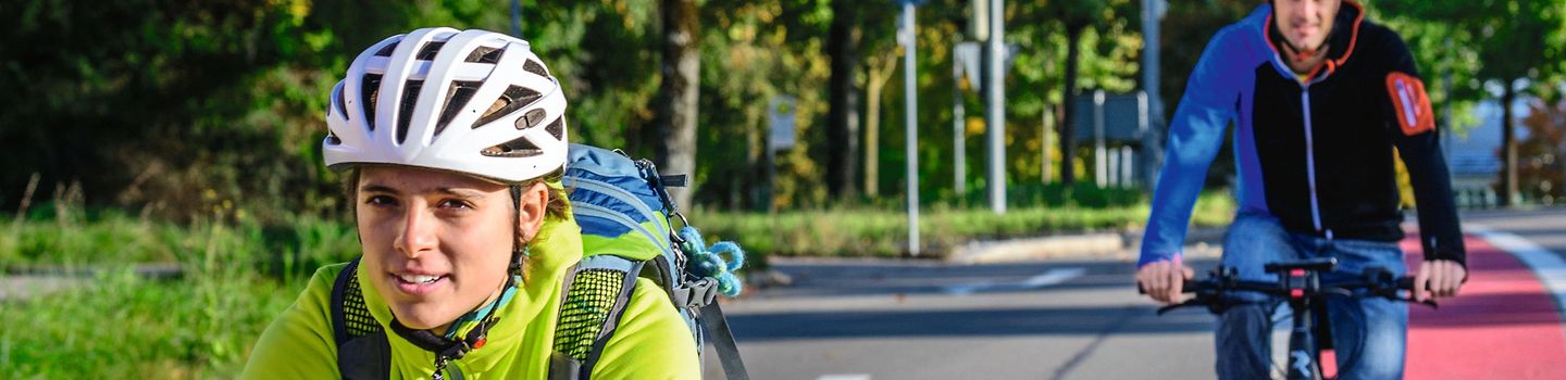 Zwei Radfahrende mit Helm fahren einem farbig markierten Radweg entlang.