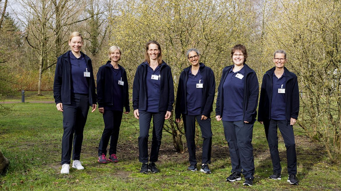 Mehrere, dunkelblau gekleidete Frauen stehen nebeneinander auf einer Wiese im Frühling.Mitglieder des medizinisch-therapeutischen Teams im BGW Rückenkolleg am BG Klinikum Hamburg (Carola Eischleb; Doerthen Prieg-Hoersch, Christine Nölicke, Ria Bleich, Alexandra Paulzen, Niela Rupprecht, Constanze Fricke: Susanne Ebell (?)