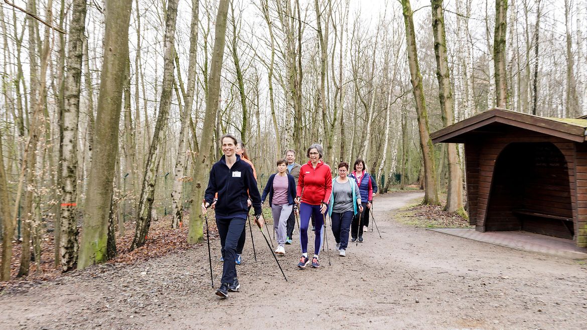 Eine Gruppe von Teilnehmenden des BGW Rückenkollegs nimmt an einer Nordic-Walking-Runde auf dem Gelände des BG Klinikums Hamburg unter Anleitung einer Trainerin teil.
