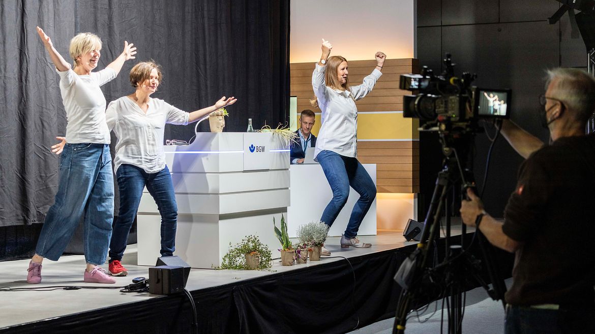 Drei Frauen machen Posen auf einer Bühne und werden dabei gefilmt.