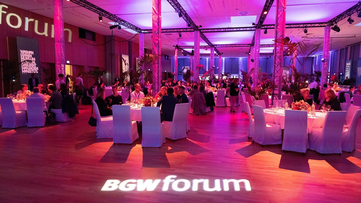 Netzwerkabend auf dem BGW forum: Menschen sitzen an gedeckten Tischen. Der Raum ist violett beleuchtet.