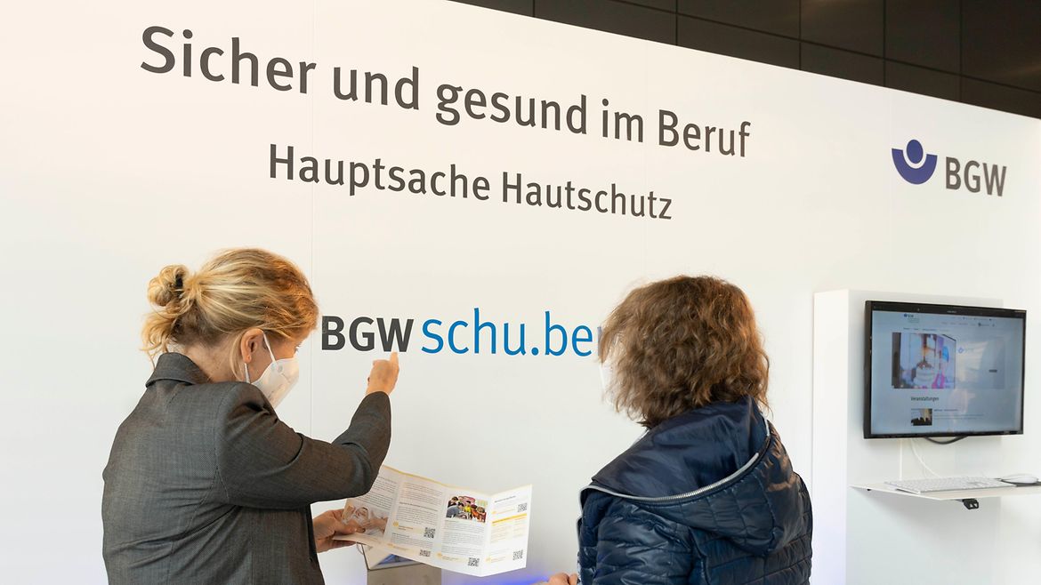 Zwei Frauen stehen am BGW-Hautschutzstand und schauen zusammen in einen Flyer.
