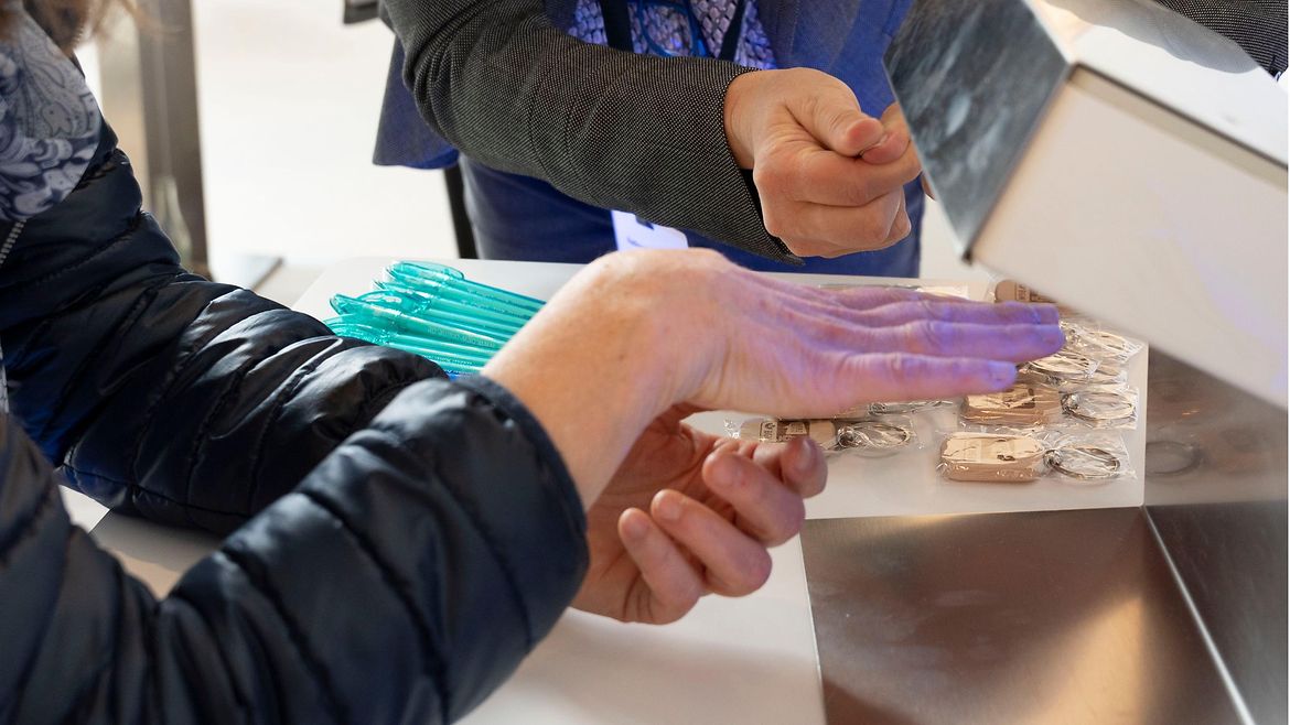 Zwei Frauen schauen sich ein Dermalux-Gerät an. Eine von ihnen hält ihr Hand unter das UV-Licht.