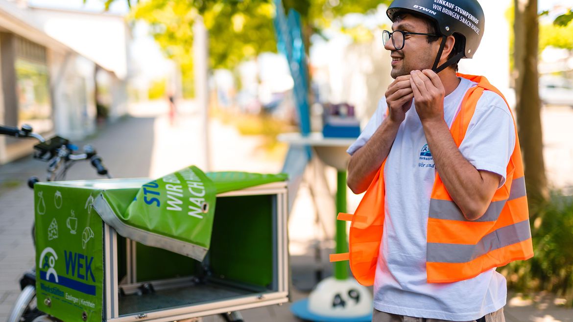 Junger Mann mit Warnweste, Helm steht neben einem Lastenrad. Er löst die Befestigung seines Helms.