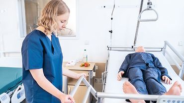 BGW test Eine Person in Pflegekleidung betätigt das Bettgitter eines Pflegebetts - im Bett liegt ein Patienten-Dummy.
