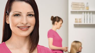 Unterrichtsmaterial zu "Eine Ausbildung, die passt" Junge Friseurin im Vordergrund, eine weitere Friseurin schneidet im Hintergrund die Haare einer Kundin
