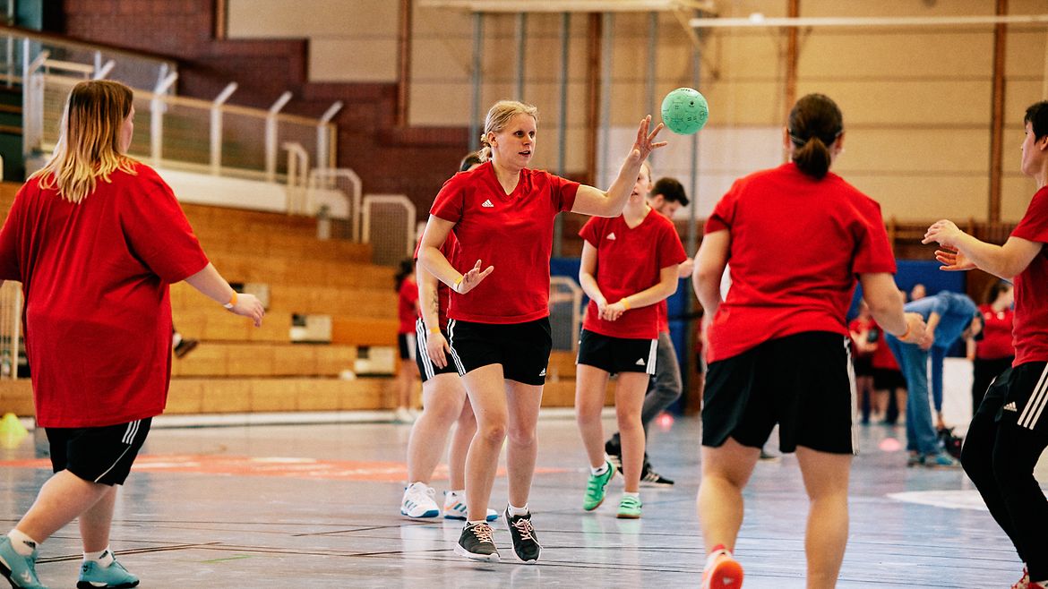 Fünf Handballerinnen auf einem Spielfeld werfen sich den Ball zu.