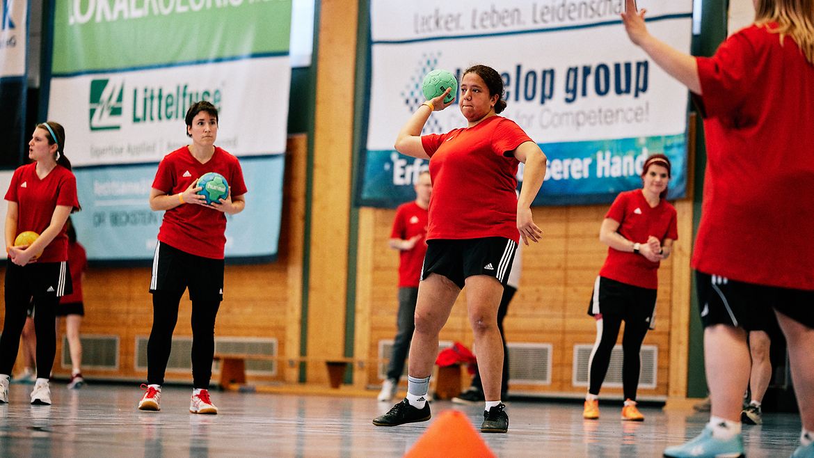 Fünf Handballerinnen auf einem Spielfeld werfen sich Bälle zu.